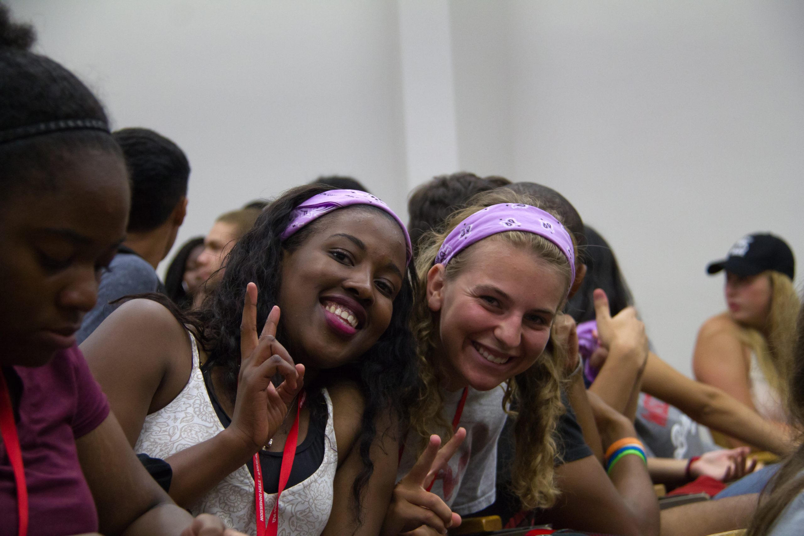 Two students lean together, smiling and giving peace signs to the camera.