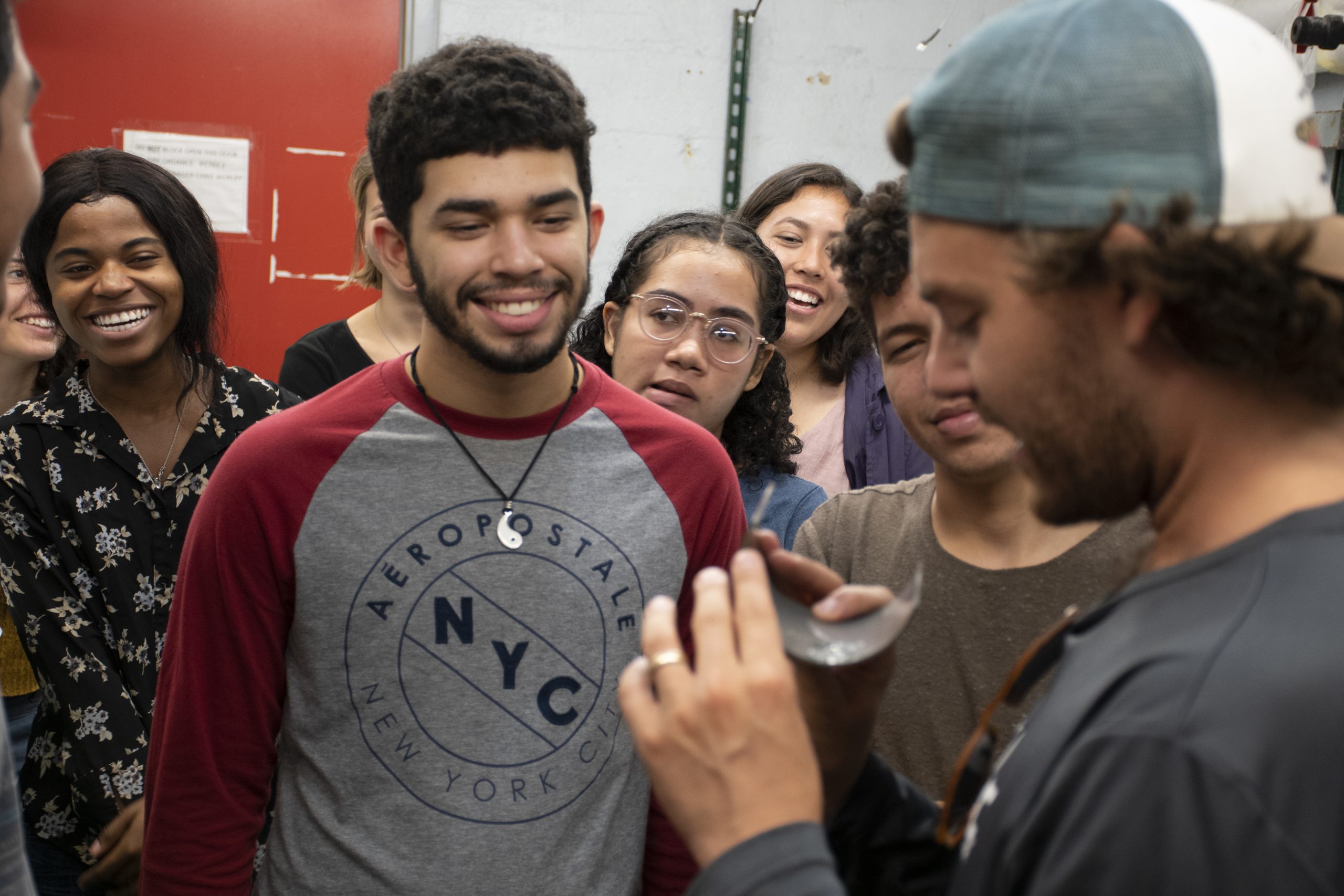 A student hold up an object to show another student, while several other students look on.