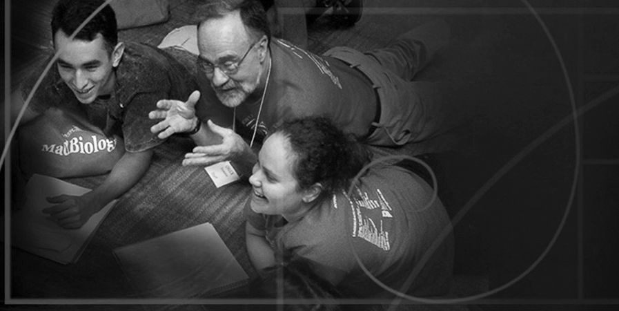 In a black and white photo, a professor and two students are lying on their stomachs on the floor, propped up on their elbows, talking and smiling. A geometric diagram of the golden ratio is superimposed on the photo. 
