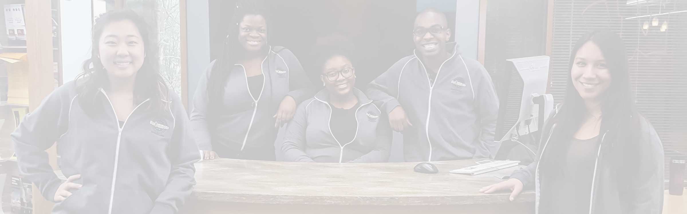 Five students sit and stand around a table, smiling at the camera.