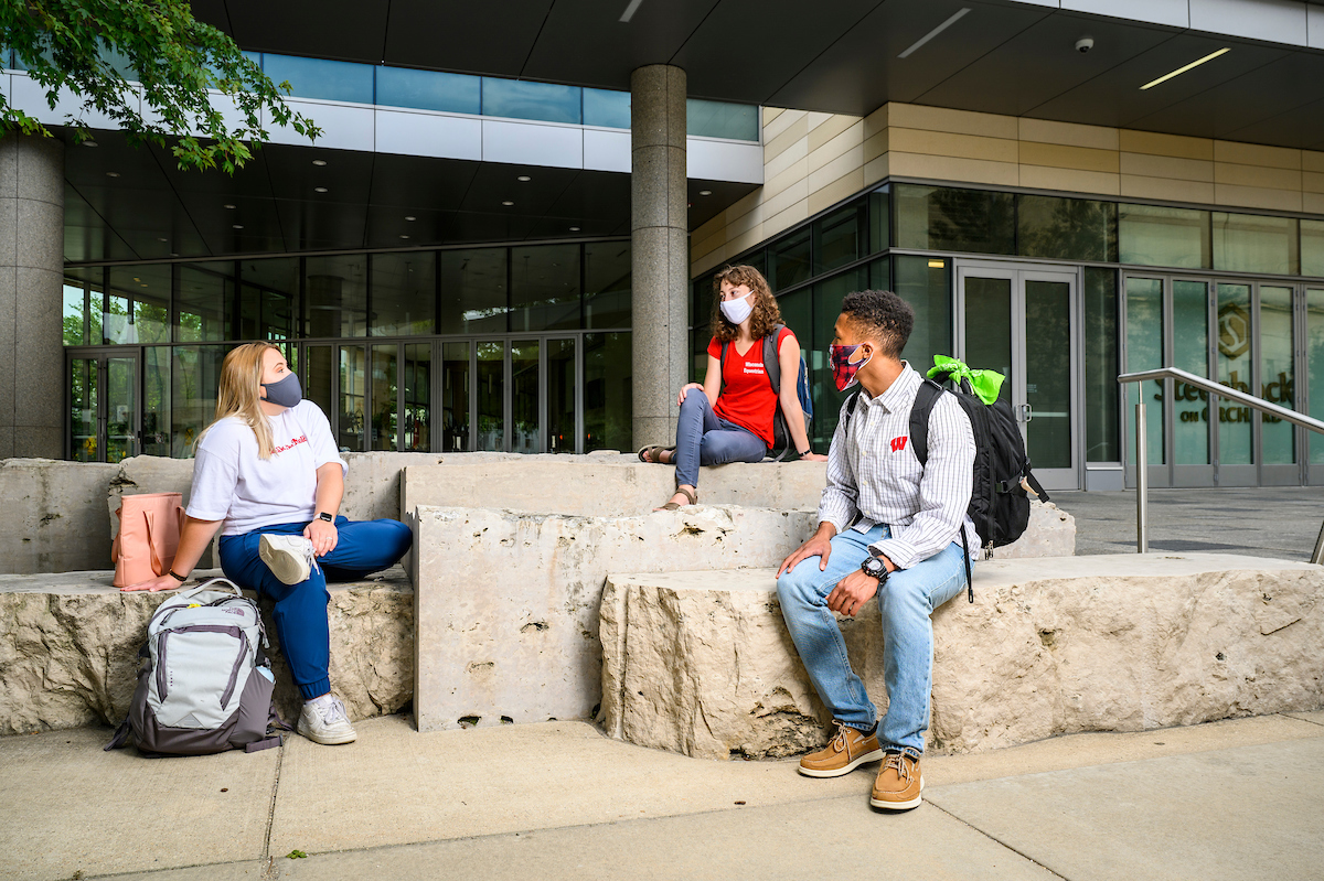 Three students wear masks and maintain physical distance to demonstrate safe gathering during the COVID-19 pandemic.