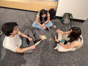 Three students play a game of Uno while sitting cross-legged on the floor.