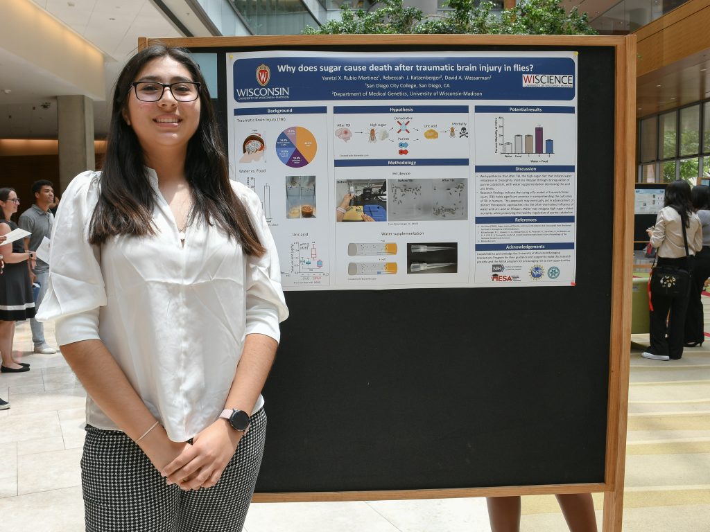 Yaretzi Martinez, a student in the summer research program, stands smiling next to her research poster. 