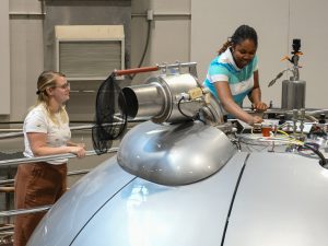 Tow students work on a project on a large machine Inside the National Magnetic Resonance Facility at UW–Madison. 