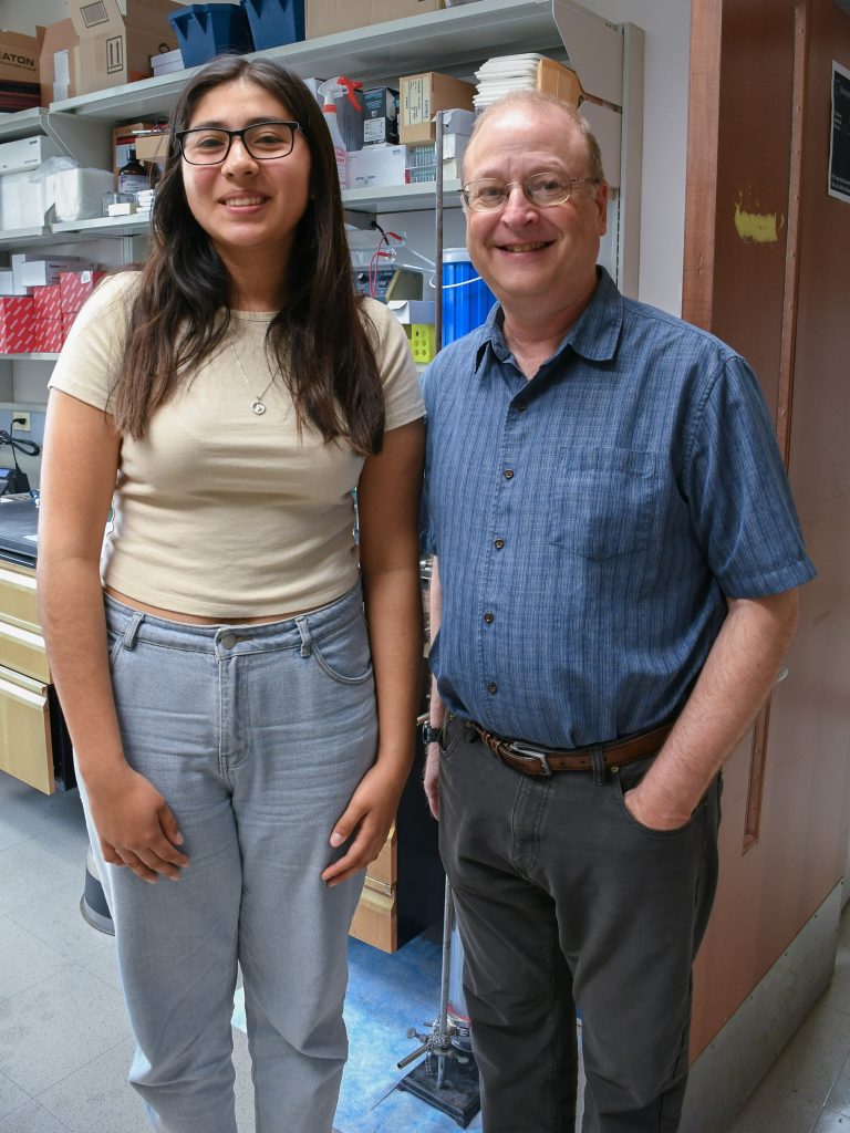 A student and a professor stand together in a science lab. 