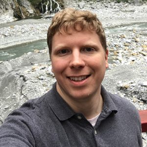 Headshot of Aaron Hoskins with a rocky riverbed in the background.