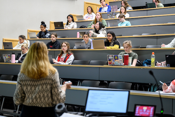 A professor stands in front of a lecture hall partially filled with students.