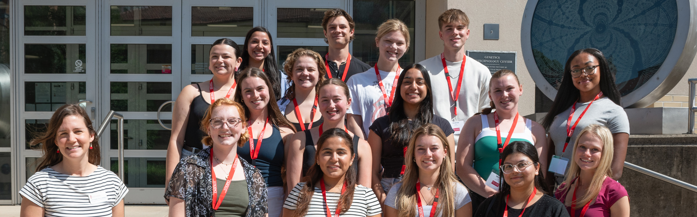 About 16 WISCIENCE Peer Leaders stand smiling with Cara Theisen, Director of Professional Development in Teaching & Learning at WISCIENCE.