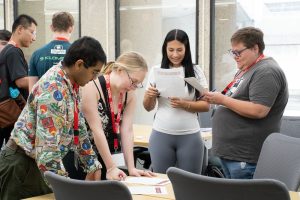 Several transfer students, along with WISCIENCE Peer Leader Valeria Diaz Moreno, hold paper and pen and mingle as they ask each other questions about themselves.