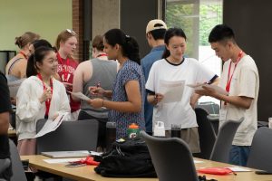 Several transfer students holding paper and pen mingle as they ask each other questions about themselves.