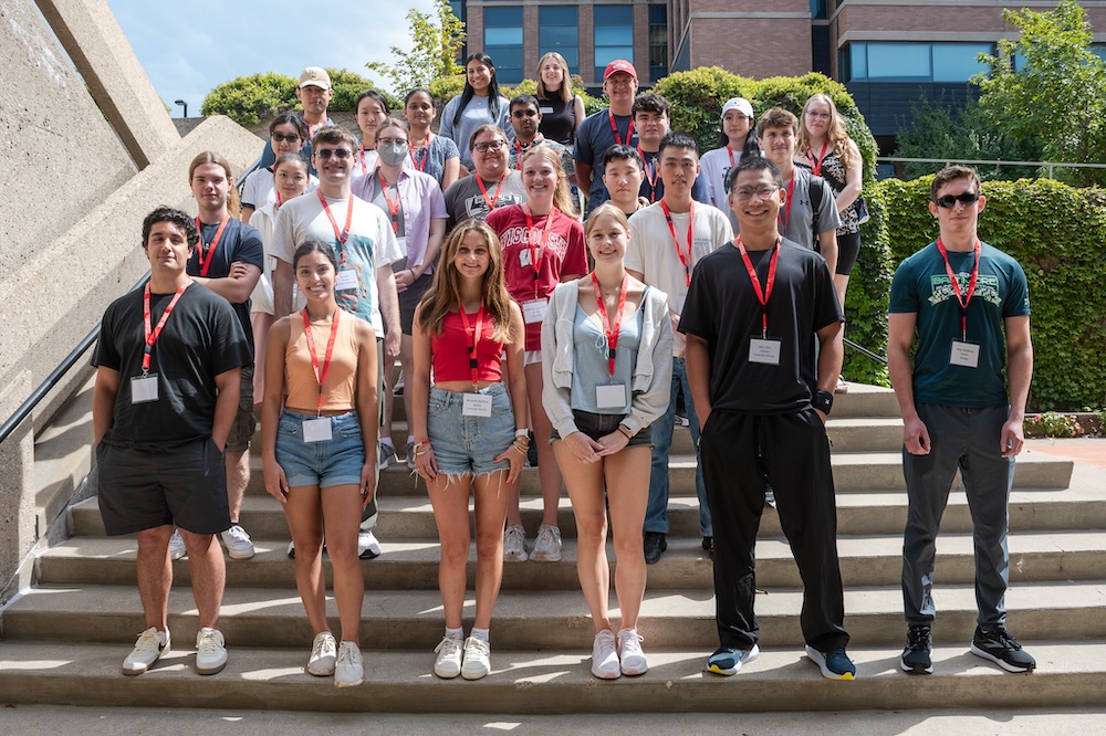 About two dozen STEM transfer students wearing red WISCIENCE lanyards stand together on the stairs of Steenbock Library.