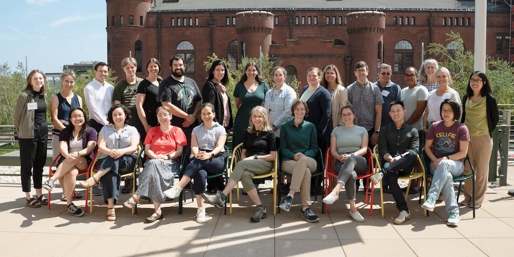 A group of about 25 biology educators from across the US sit and stand together outdoors in front of a building. 