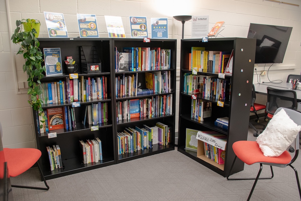 Three medium-sized black bookshelves full of books plus a floor lamp and two chairs.