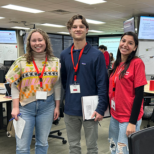 Three peer leaders wearing lanyards pose together in a classroom.