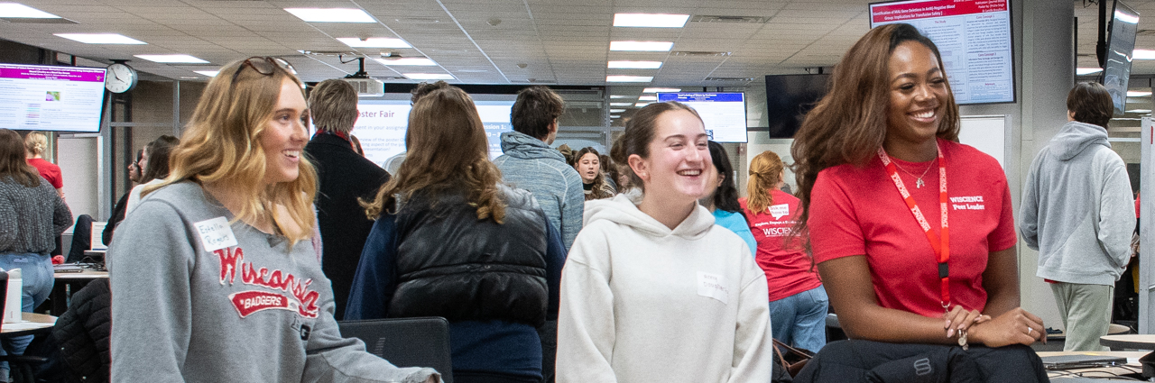 Two students and a peer leader stand next to a table smiling.