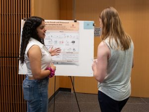 Gabriela P. Romero-González, a summer research program student, stands in front of her research poster while explaining her research to an onlooker. 
