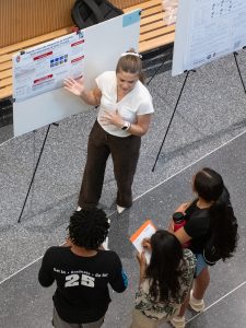 Noah Venable, a summer research program student, presents her research to three students at a poster presentation. 