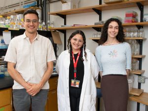 Alexia S. Meléndez Rivera, a summer research student, stands in the lab next to her mentor, Noah Brown, and PI, Emile Gluck-Thaler. All three are smiling at the camera. 