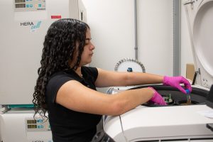 Gabriela P. Romero-González, a summer research program student, places a test tube in a machine in the lab. 