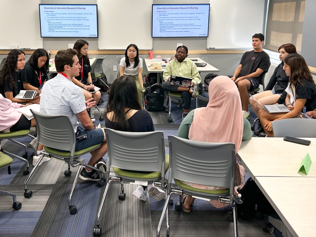 Several students and an instructor sit in a circle in a classroom.