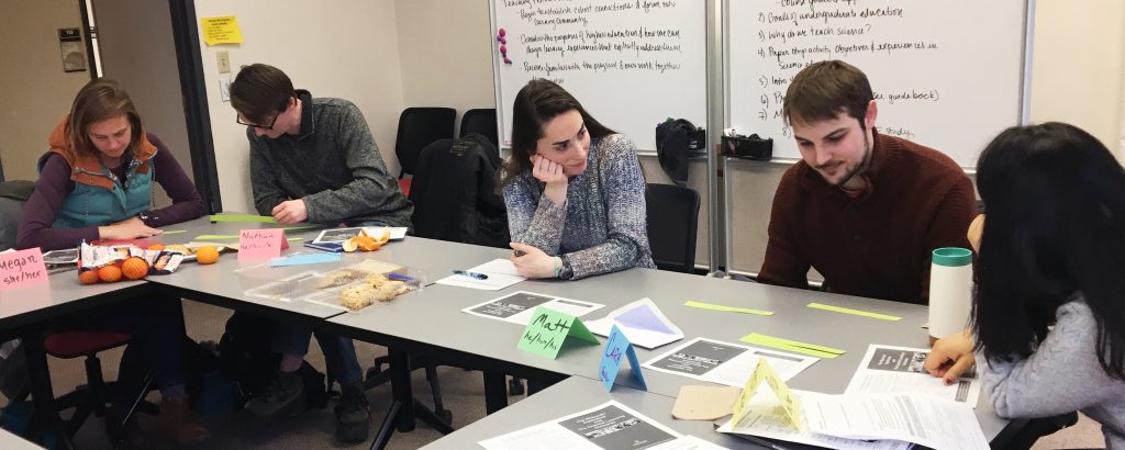 Five students in the Scientific Teaching Fellows program sit at classroom tables doing work in small groups. 
