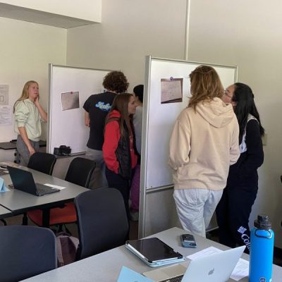 Students in Exploring Service in STEM (INTEGSCI 140) discuss class topics at whiteboards around the classroom.