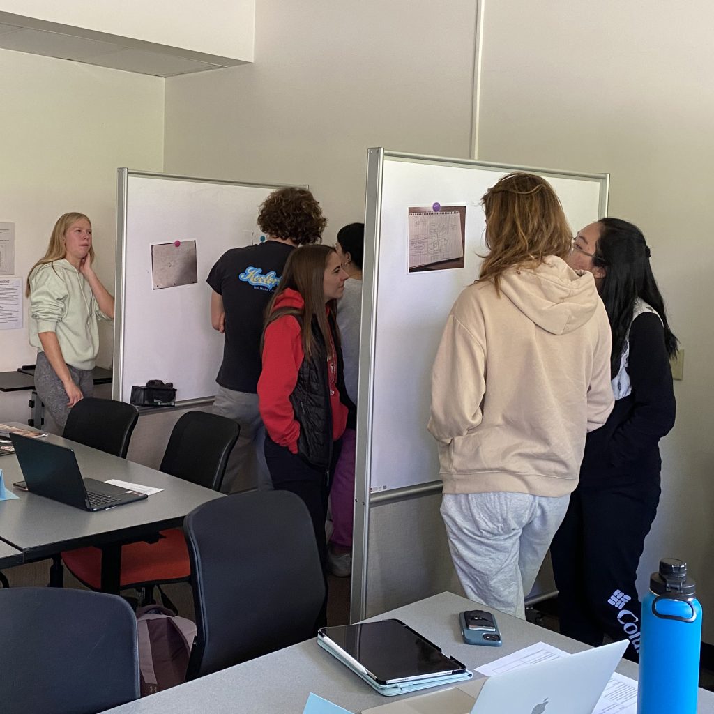 Students in Exploring Service in STEM (INTEGSCI 140) discuss class topics at whiteboards around the classroom.