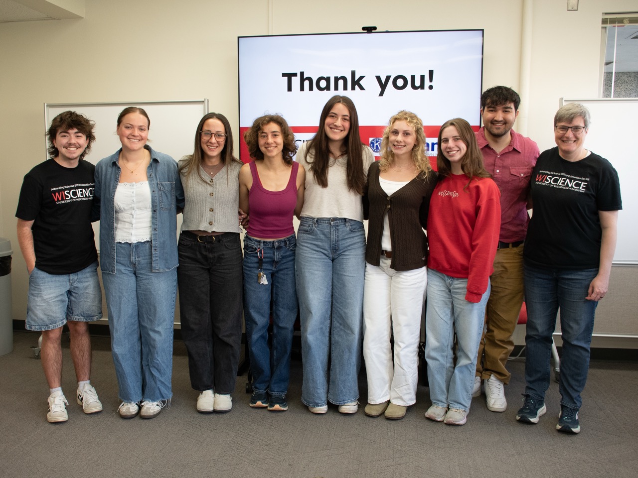 Seven students, a Peer Leader, and course director Anna Courtier stand smiling in a row in front of a screen that reads, "Thank You!"