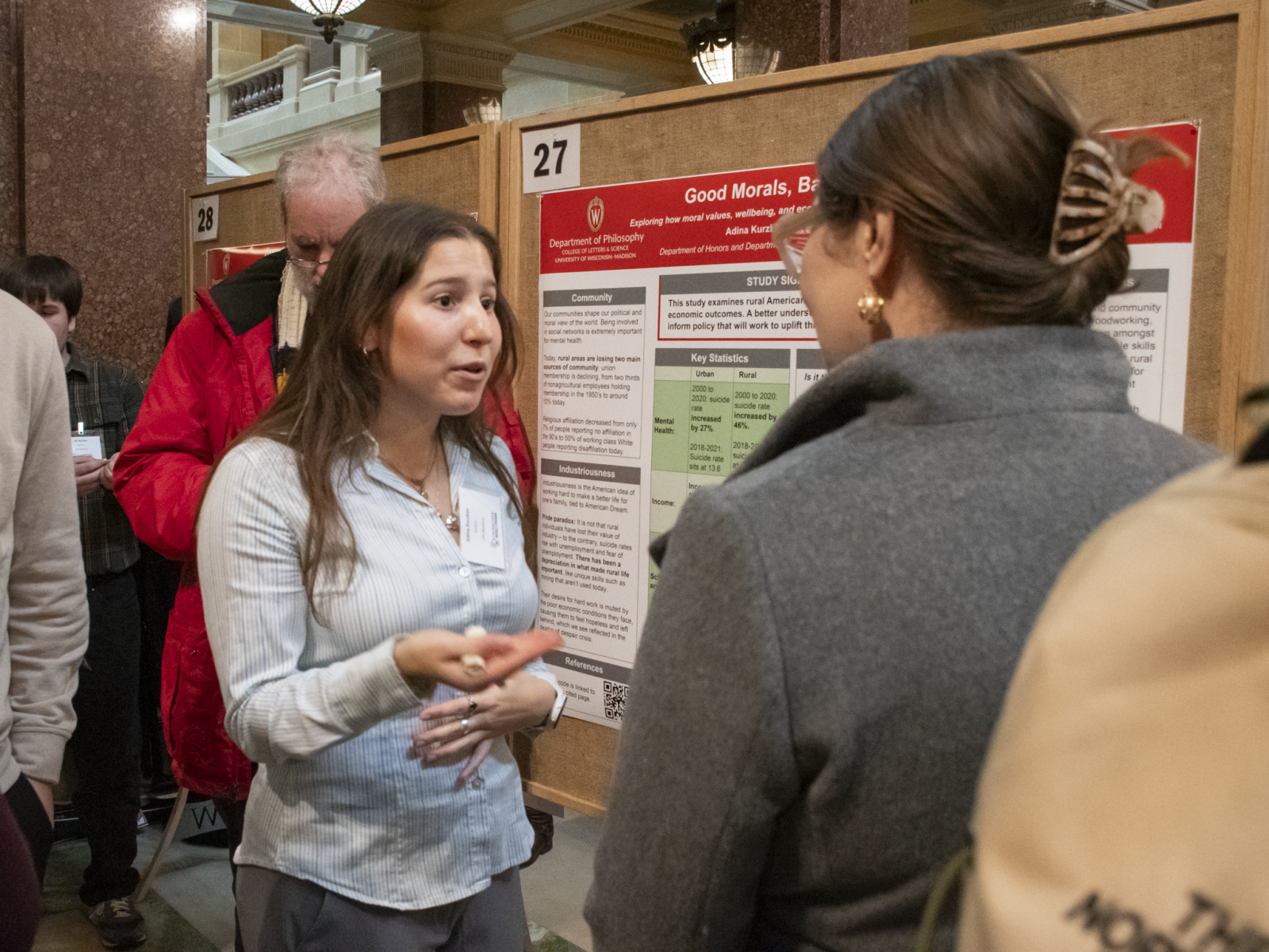 A student researcher presents her poster at Research in the Rotunda while an attendee looks on.