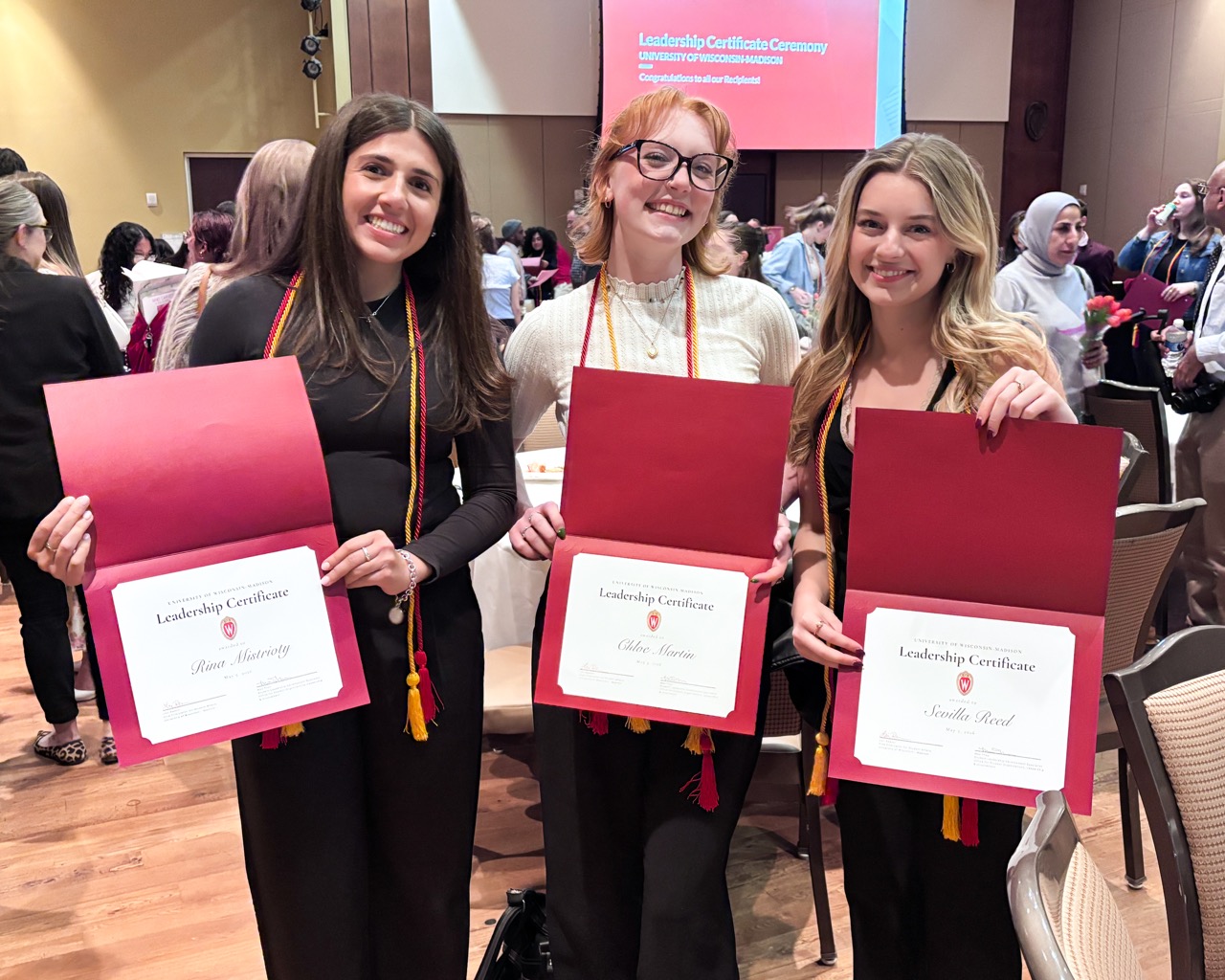 Three students smile while holding red folders containing their Leadership Certificates.