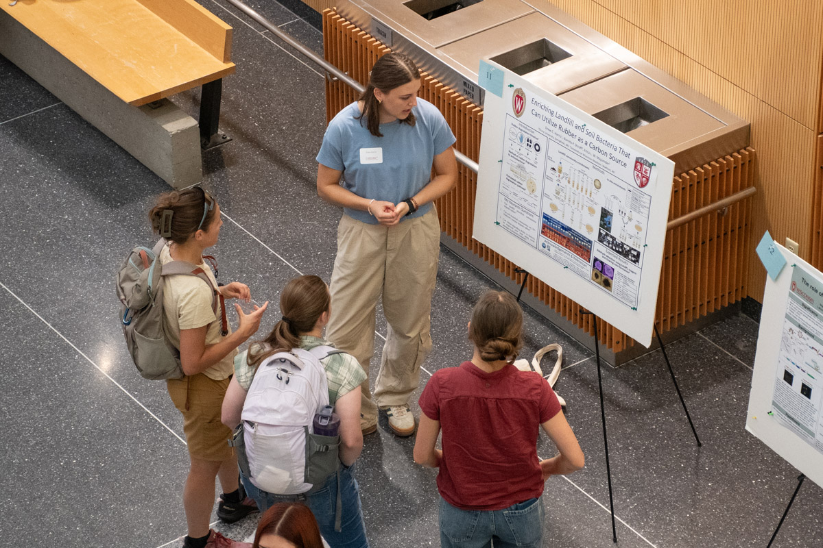 A student presents her research poster to three viewers.
