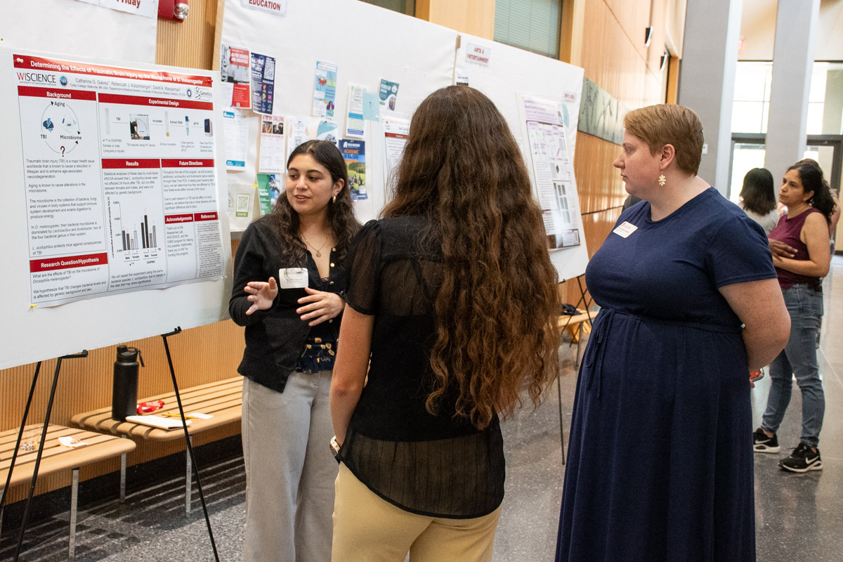 A student presents her research poster to two onlookers.